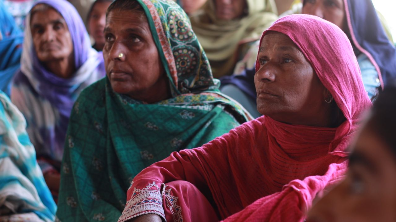 South Asian women in colorful traditional clothing attentively participating in a village meeting.