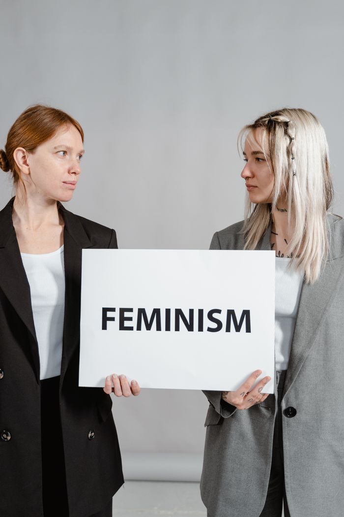 Two women in business attire holding a feminism sign, promoting empowerment and gender equality.