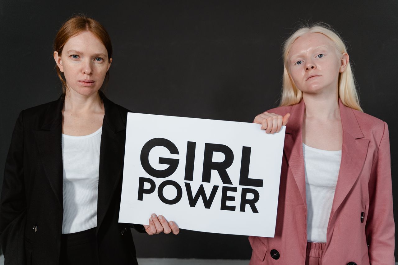 Two women stand confidently holding a 'Girl Power' sign, symbolizing empowerment and equality.